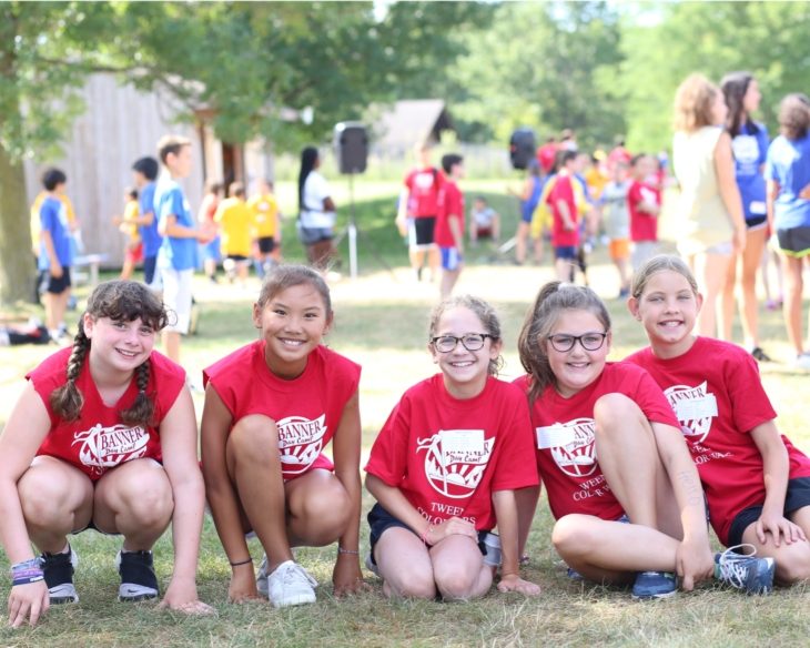 Group of girl campers all in banner day camp shirts smiling on the grass together