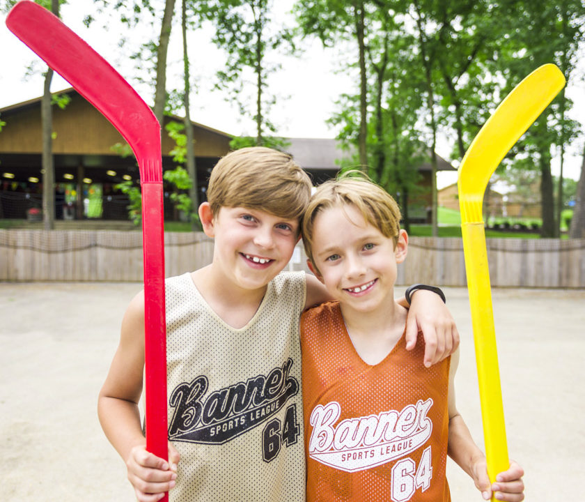 Two boy campers holding hockey sticks and smiling together