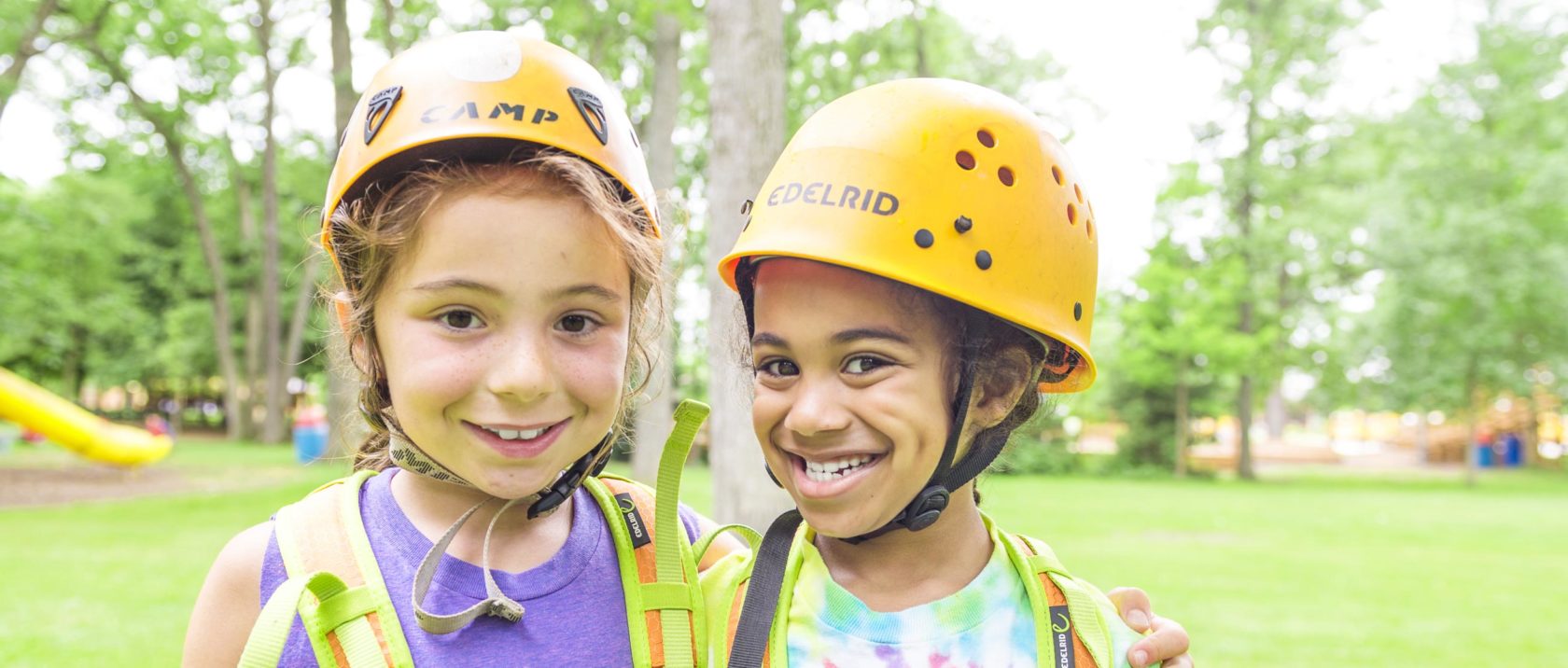 Two girl campers with zipline gear on smiling together