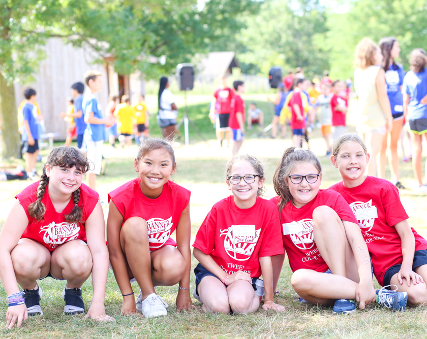 Group of girl campers sitting on grass together in matching red shirts