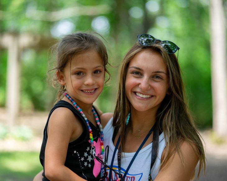 Female counselor holding a girl camper and smiling