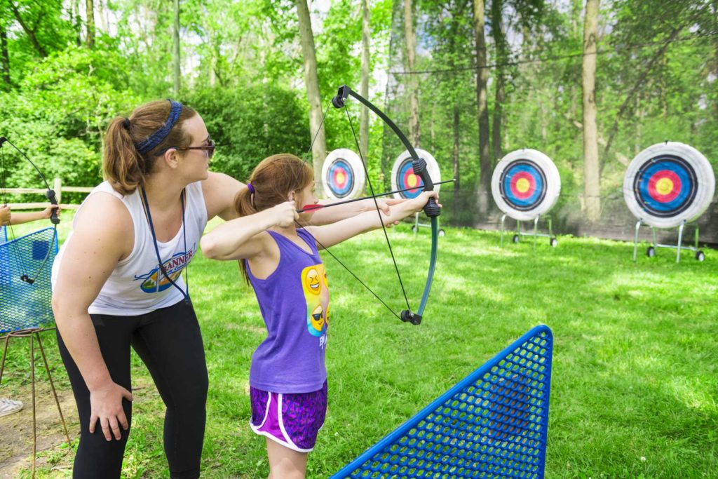 A counselor helping a camper aim and shoot an arrow