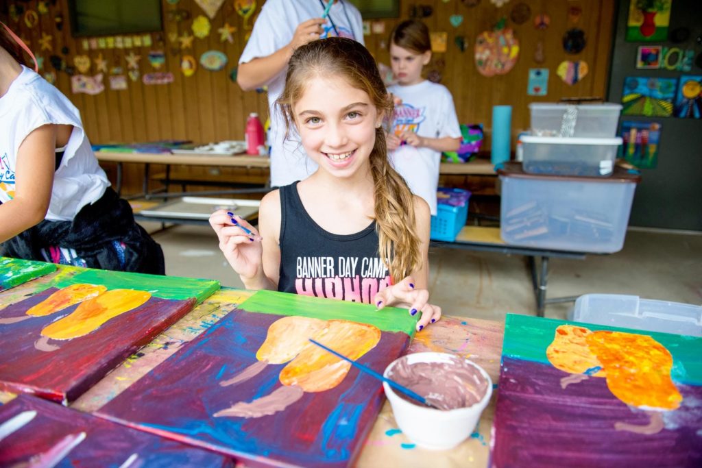 A girl smiles as she paints fruit