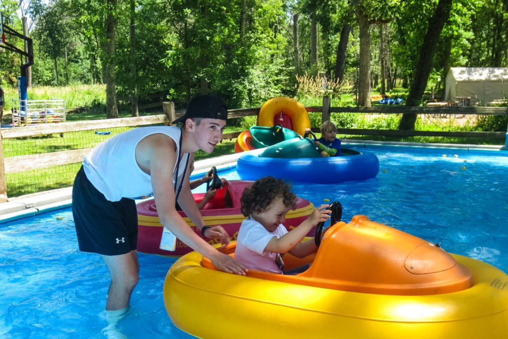 A counselor pushes a young camper along in an orange and yellow bumper boat