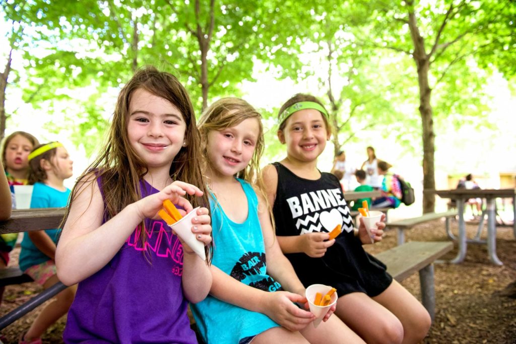 Three girls sit outside eating and smiling