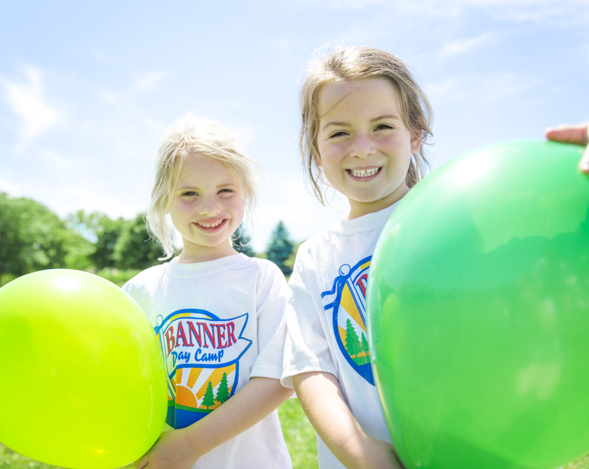 Two girl campers smiling holding balloons