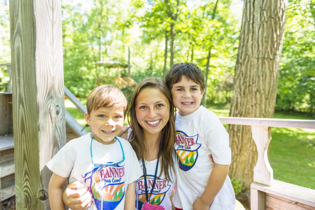 A counselor smiling with two little campers