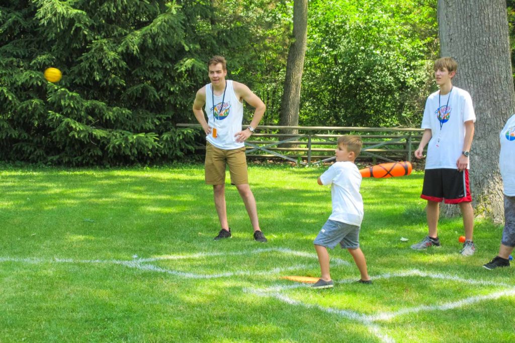 A young boy playing baseball with two counselors as umpires