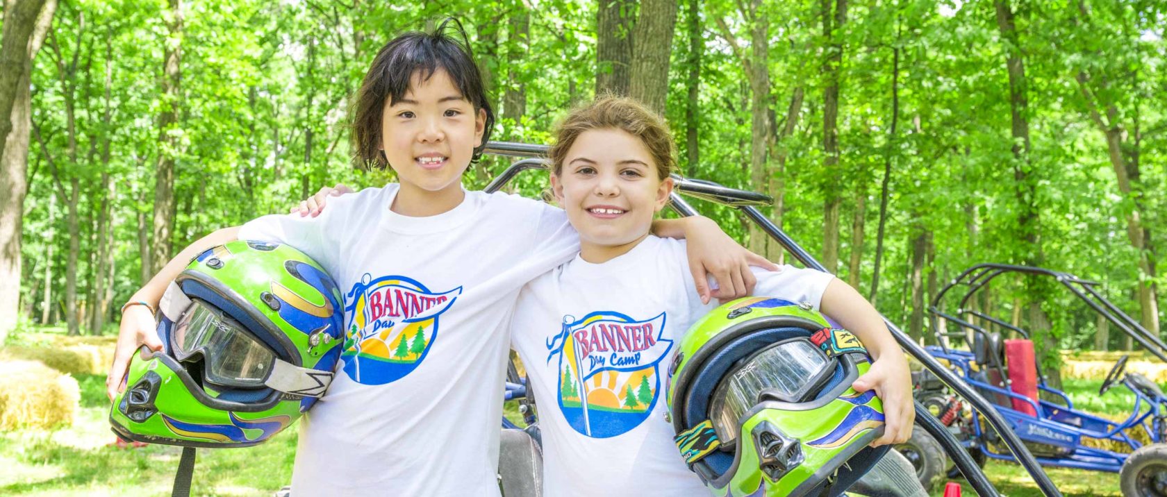 Two girl campers with go kart helmets in their hands smiling together