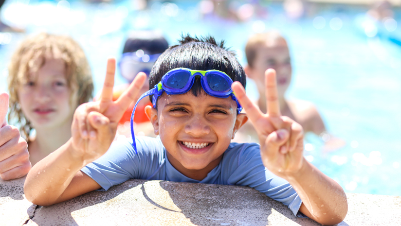 Boy camper giving peace signs in the pool