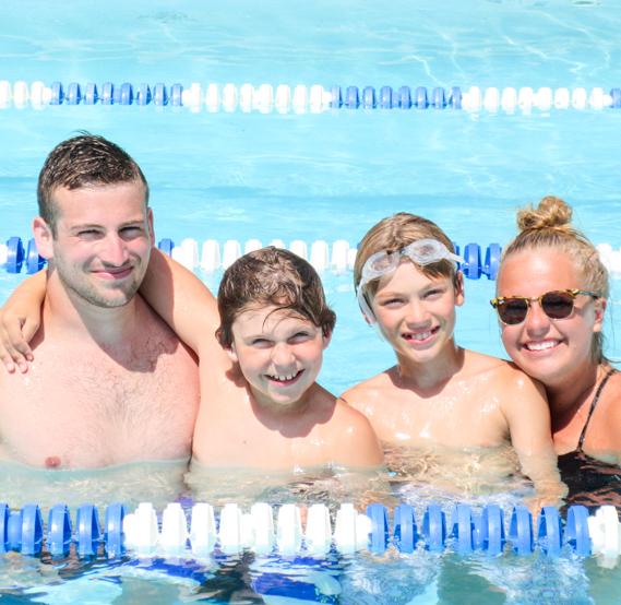 Two boy campers smiling in the pool with two staff members