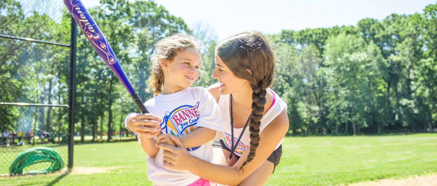 Staff member teaching a girl camper how to swing a softball bat