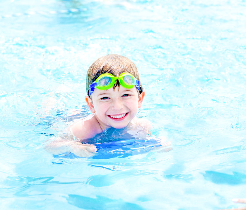 Boy camper smiling as he swims in the pool