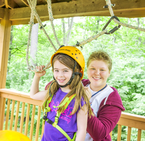 Female staff member helping a girl camper with the zipline