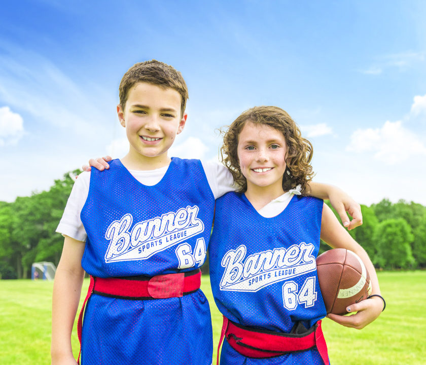 Two boys smiling together on the football field holding a football