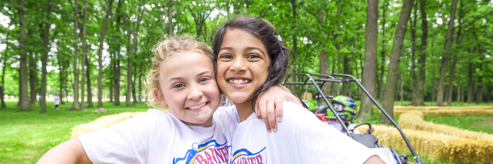 Two girl campers smiling with arms around each other on the go-kart course