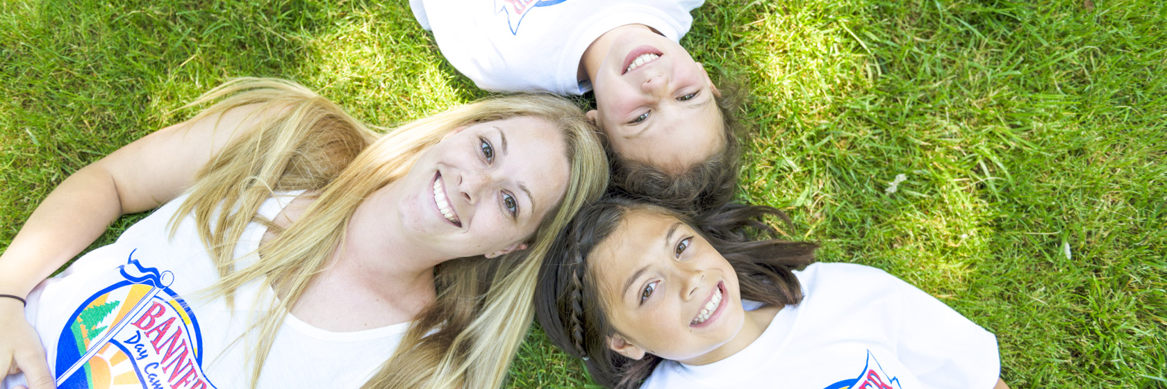 Female counselor and two girl campers laying on the grass together with they heads together in a circle