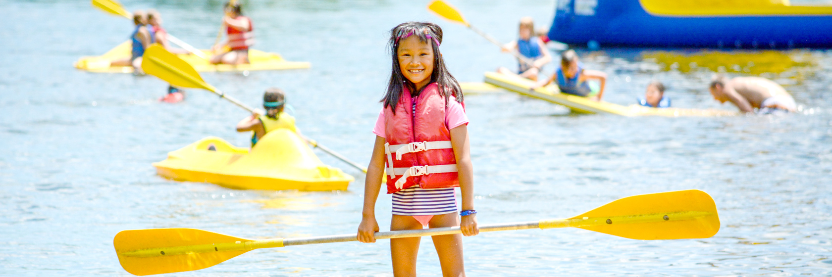 Girl camper standing up on a paddleboard in the lake smiling