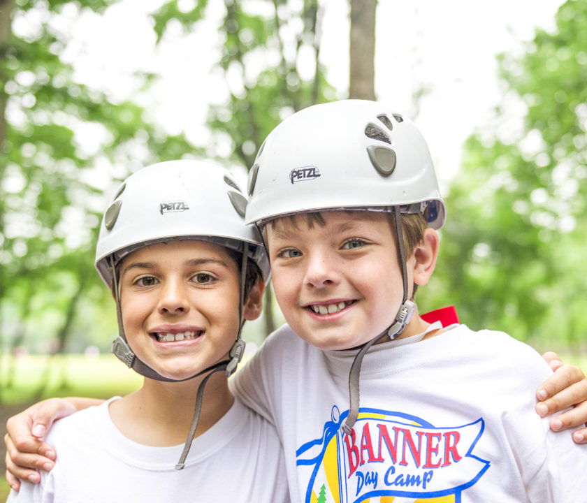 Two boy campers in helmets at the ziplining station smiling together