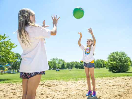 Two girl campers playing volleyball on the sand