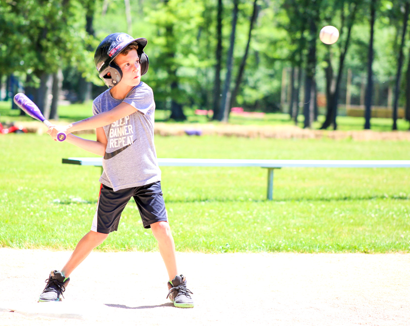Senior boy camper swinging at a baseball with a bat