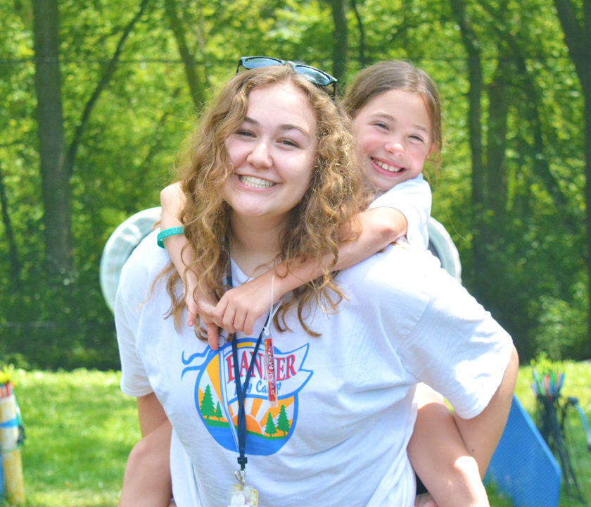 Female CIT camper giving a young girl a piggy back ride