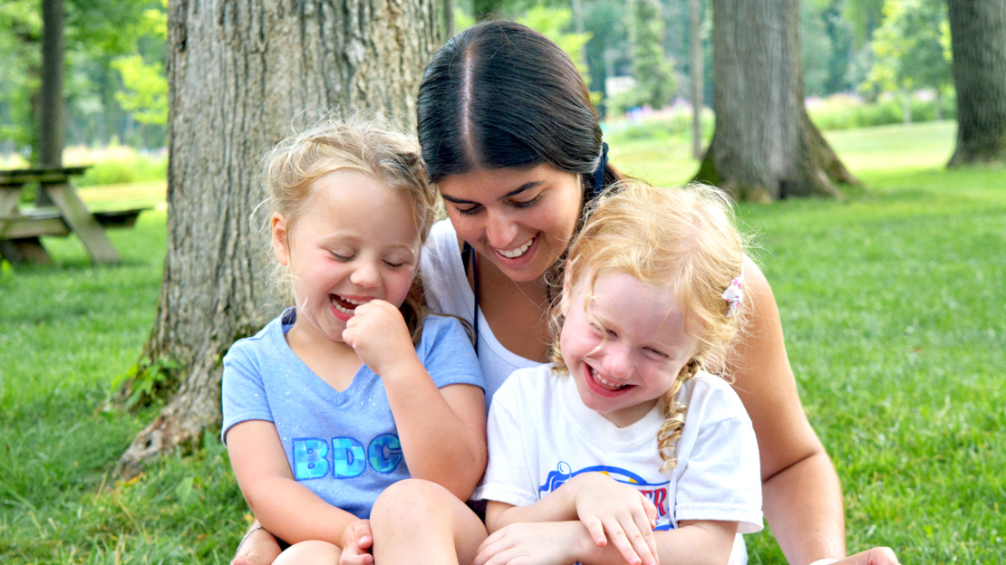 Female counselor with two young girl campers sitting on lap smiling