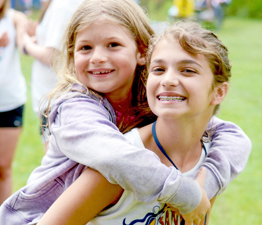 Female CIT camper giving a young girl a piggy back ride