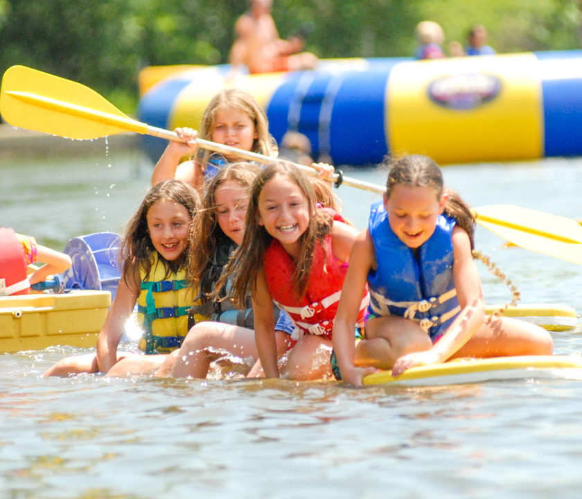 Group of girl campers sitting on a paddle board on the lake