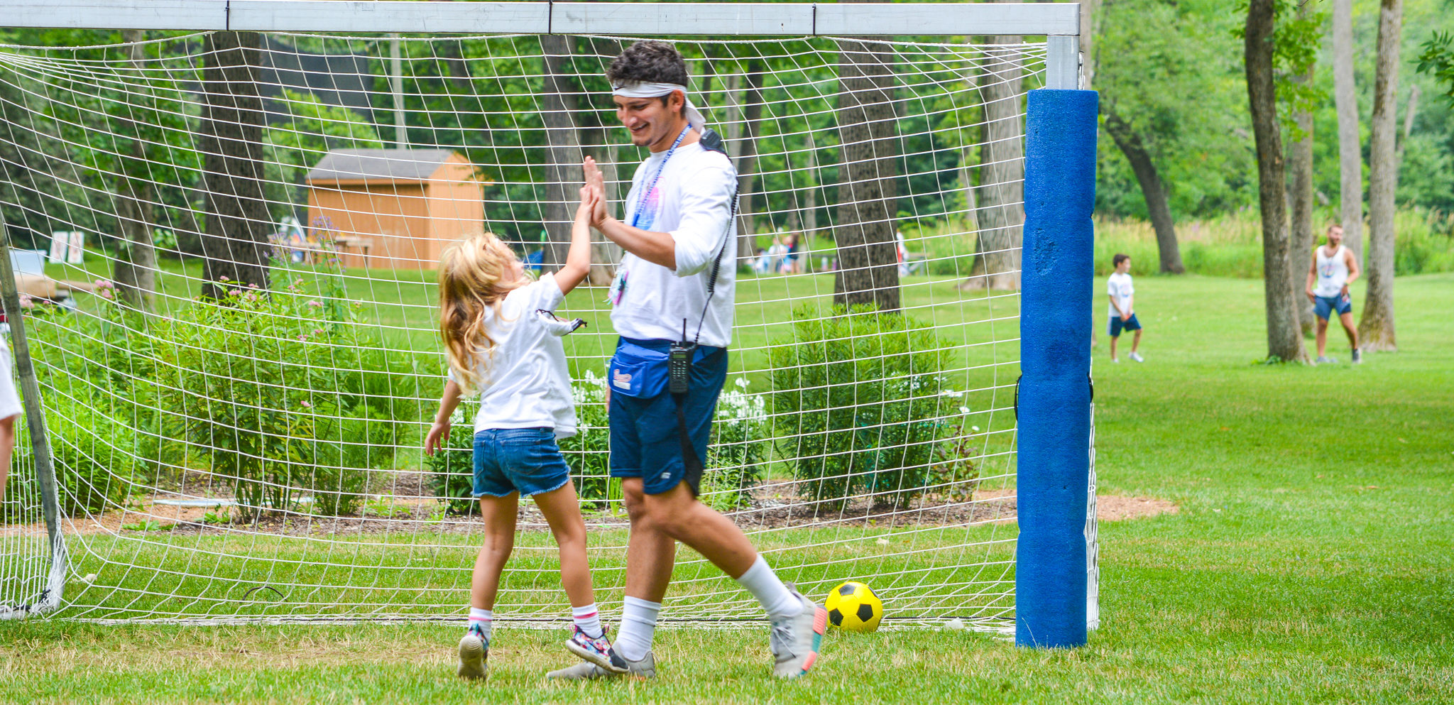 Male counselor encourages female camper while playing soccer