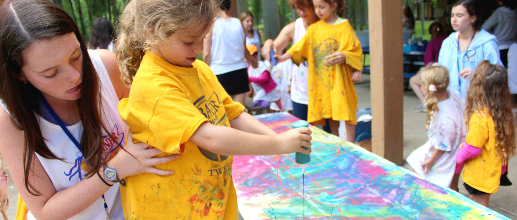 Female counselor helps female camper at arts & crafts